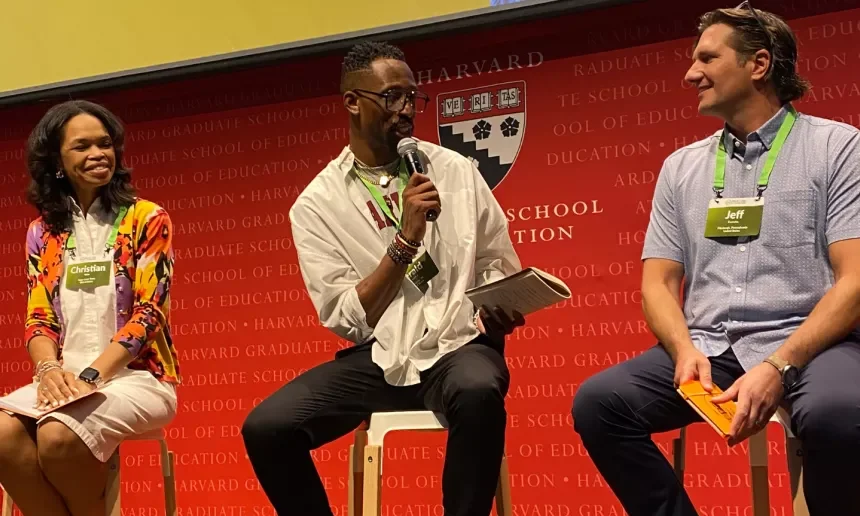 Three people sitting in stools on a speaking stage at a conference.