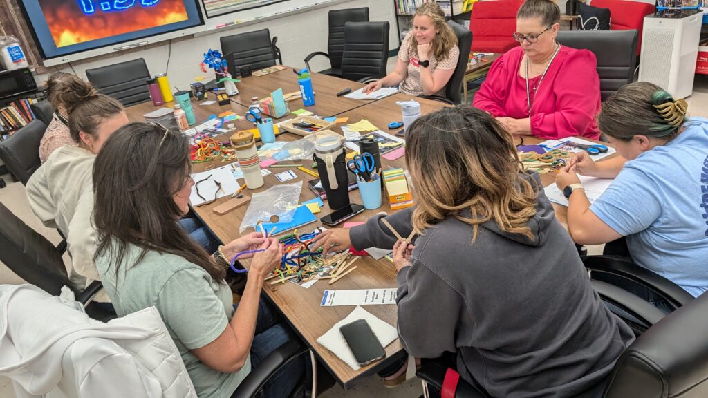 A group of women sit around a long table making crafts with pipe cleaners