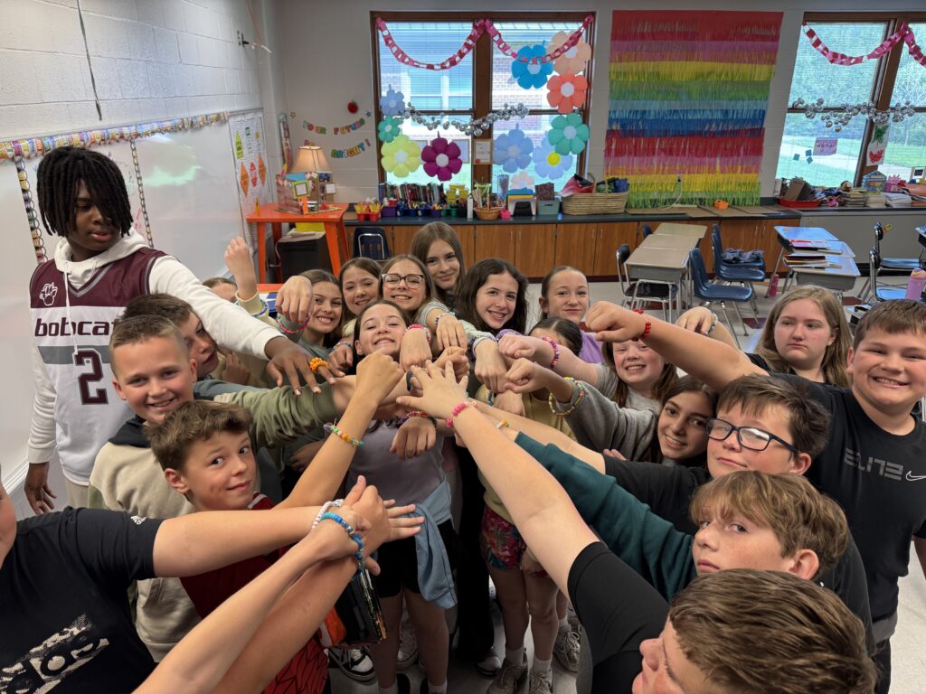 A group of middle school students put their hands together in a team circle.